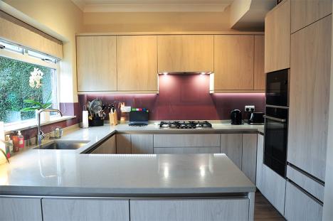 Rich purple glass splashbacks enhance the pale melamine cabinets and quartzstone worktops in this compact kitchen