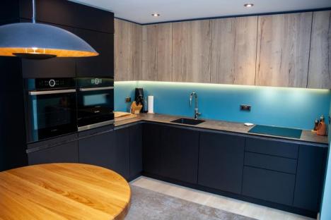 Kitchen base units in black with wall units in oak and a blue splashback in between