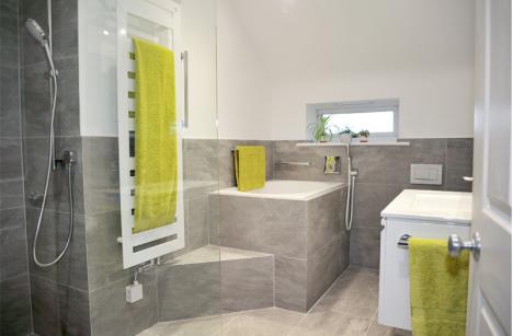 bathroom with half height grey porcelain tiles, towel radiator, deep soaking tub with step up and grab handles, vanity unit