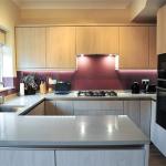 Rich purple glass splashbacks enhance the pale melamine cabinets and quartzstone worktops in this compact kitchen