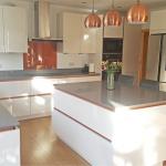 High gloss magnolia kitchen with copper handleless trim, pendant lamps with copper shades and a copper coloured splashback