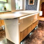 The island is fitted with fridge drawers, LED lighting and plinth spotlights. The glass worktop is supported by a steel-edged board. 