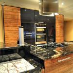 Kitchen island with high gloss Olive wood units,  tall housings behind and stainless steel  ceiling extractor above.