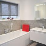 Bathroom tiled in grey porcelain tiles, bath with custom Corian® bath panel, vanity unit and illuminated mirror cabinet