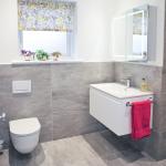 Grey tiled en-suite with wall-hung toilet and vanity unit with towel rail on the side and illuminated mirror cabinet above.